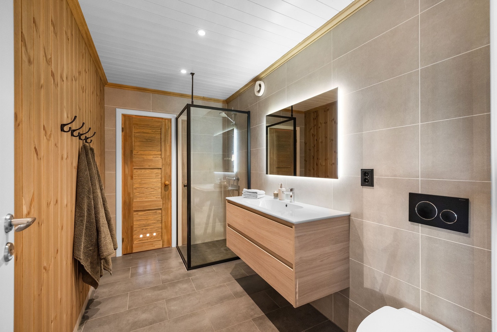 Badet fremstår som gjennomført og delikat, med en fin kombinasjon av fliser og trepanel som gir rommet både et moderne og lunt preg. Galleribilde