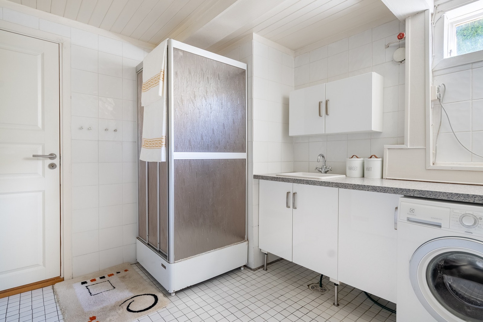 Bad/vaskerom i u. etasje med flislagte gulv- og veggflater, himling med trepanel og downlights. Innredning med slette fronter, heldekkende servant og ett-greps blandebatteri. Vegghengt toalett og dusjkabinett med skyvedør, hånddusj og regndusj. Opplegg fo Galleribilde