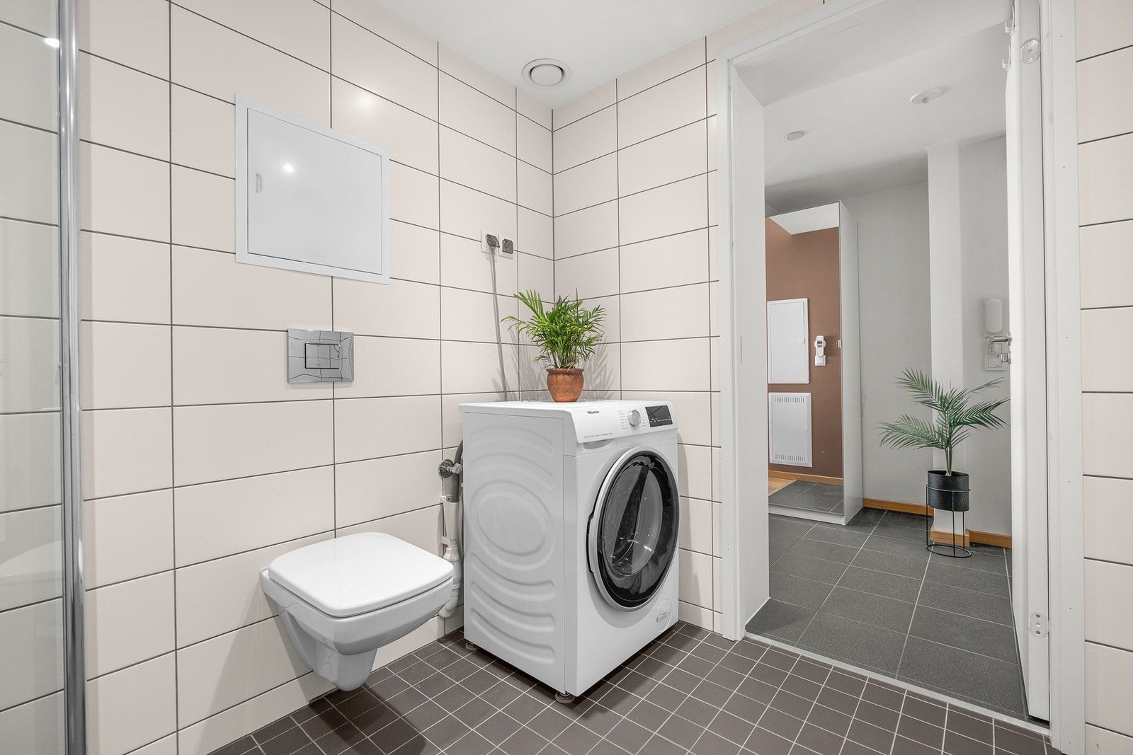 Badet er innredet med dusjhørnet, opplegg for vaskemaskin og veggmontert toalett, servantinnredning og speil med integrert belysning Galleribilde