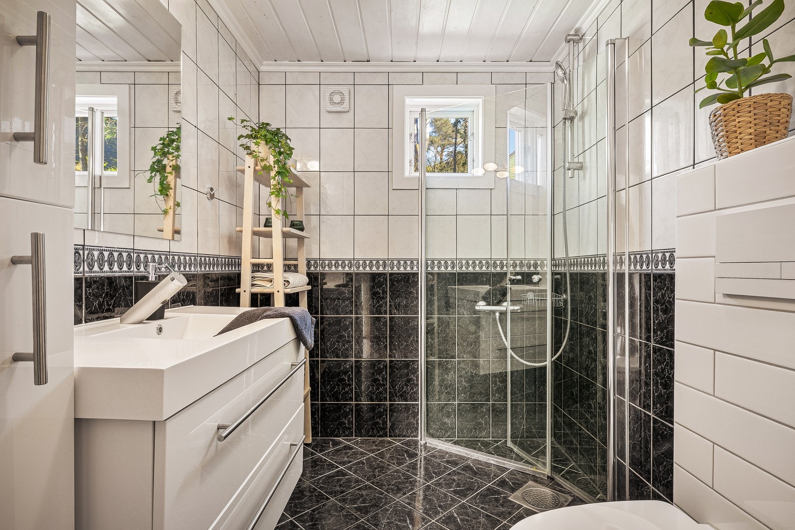 Badet har en funksjonell utforming med flislagte overflater, dusjhjørne og praktisk servantinnredning med oppbevaringsplass. Galleribilde