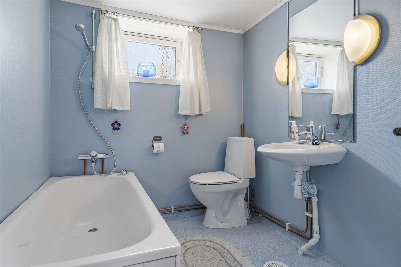 Badet i kjelleren har vinyl på gulv og malerstrie på vegger. Rommet er innredet med servant på vegg, gulvstående toalett og badekar Galleribilde