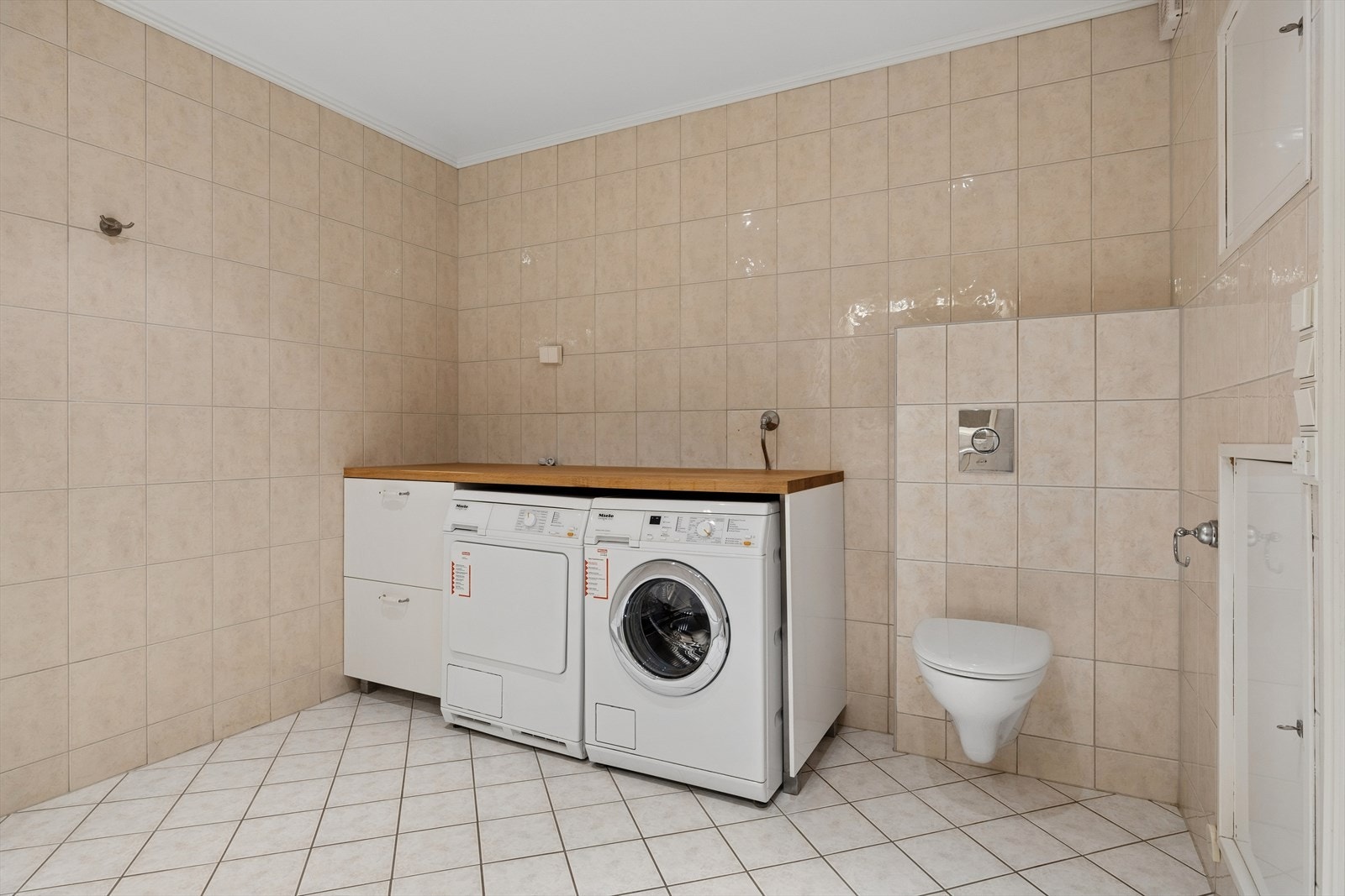Praktisk vaskeromsdel på badet med hel benkeplate og opplegg for vaskemaskin og tørketrommel. Galleribilde