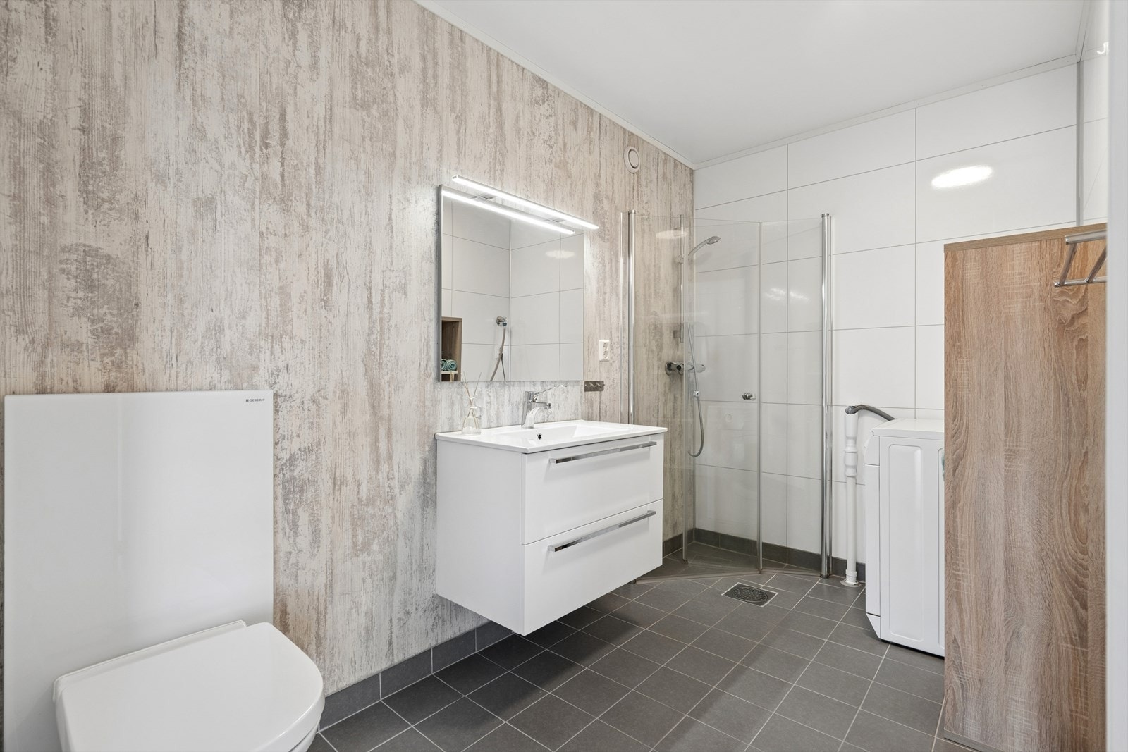 Badet i underetasjen består av servant, vegghengt speil med lys, vegghengt toalett, dusjhjørne og opplegg for vaskemaskin. Galleribilde