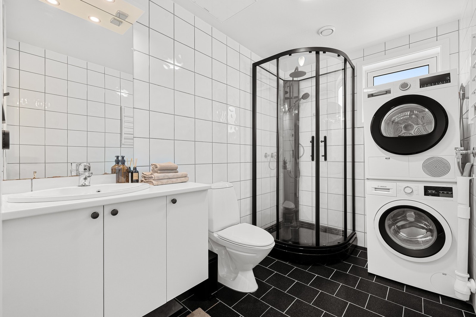 Moderne baderom utstyrt med: dusjkabinett, mekanisk avtrekk, opplegg for vaskemaskin, servant, servantskap og wc. Galleribilde