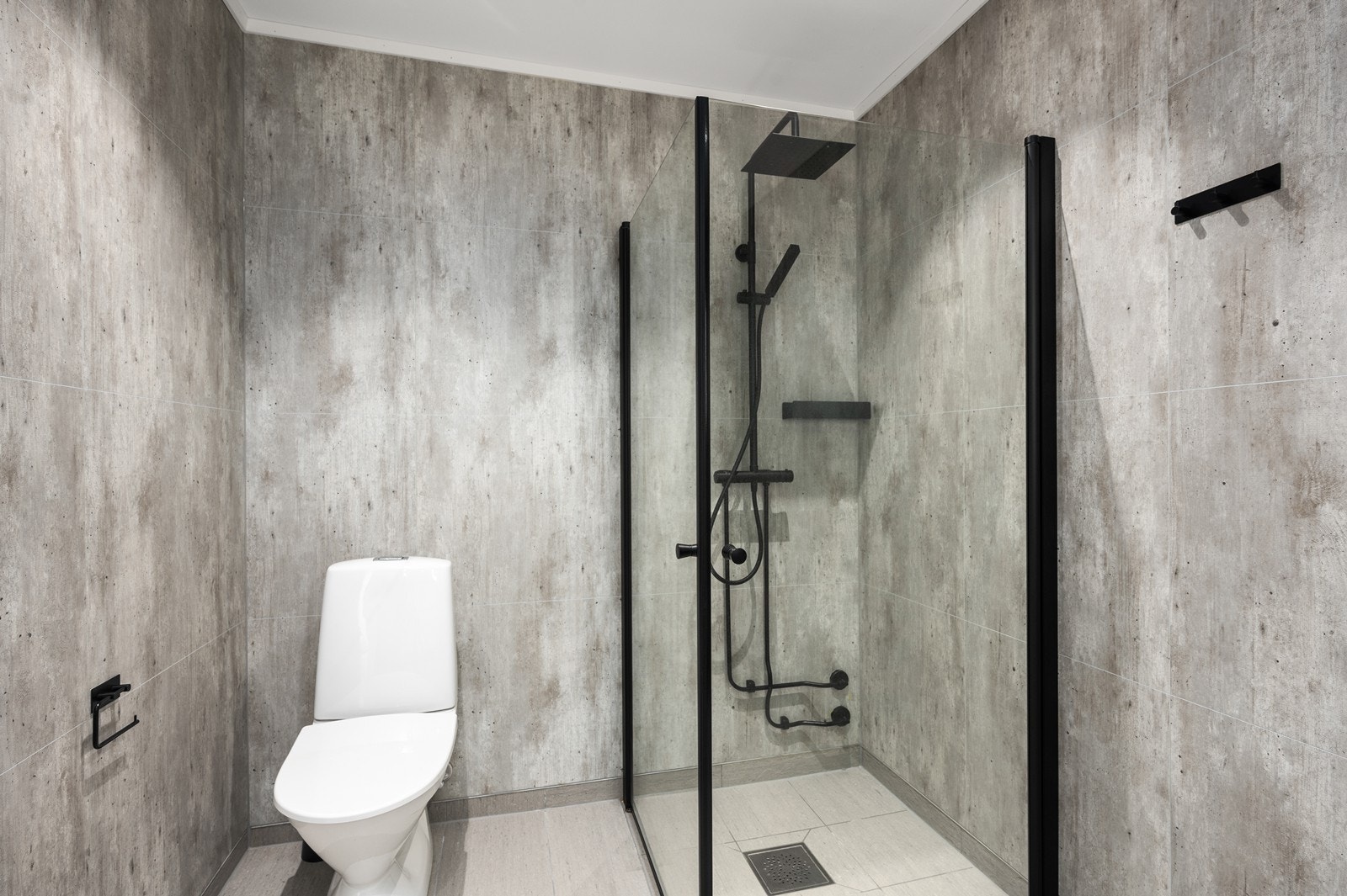 Veggene er kledd med baderomsplater og gulvet er flislagt i nøytrale fargetoner, med stilige svarte detaljer. Galleribilde
