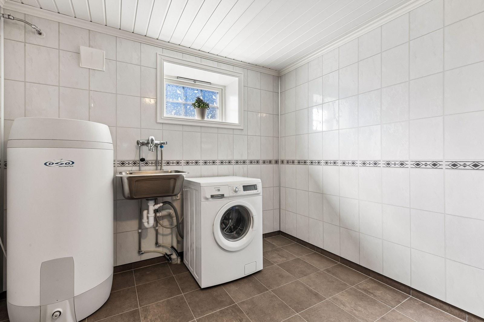 Stort og praktisk vaskerom i underetasjen med flislagt gulv, utslagsvask og opplegg for vaskemaskin. Her er det god plass til å sette opp skapløsning om man ønsker dette. Galleribilde