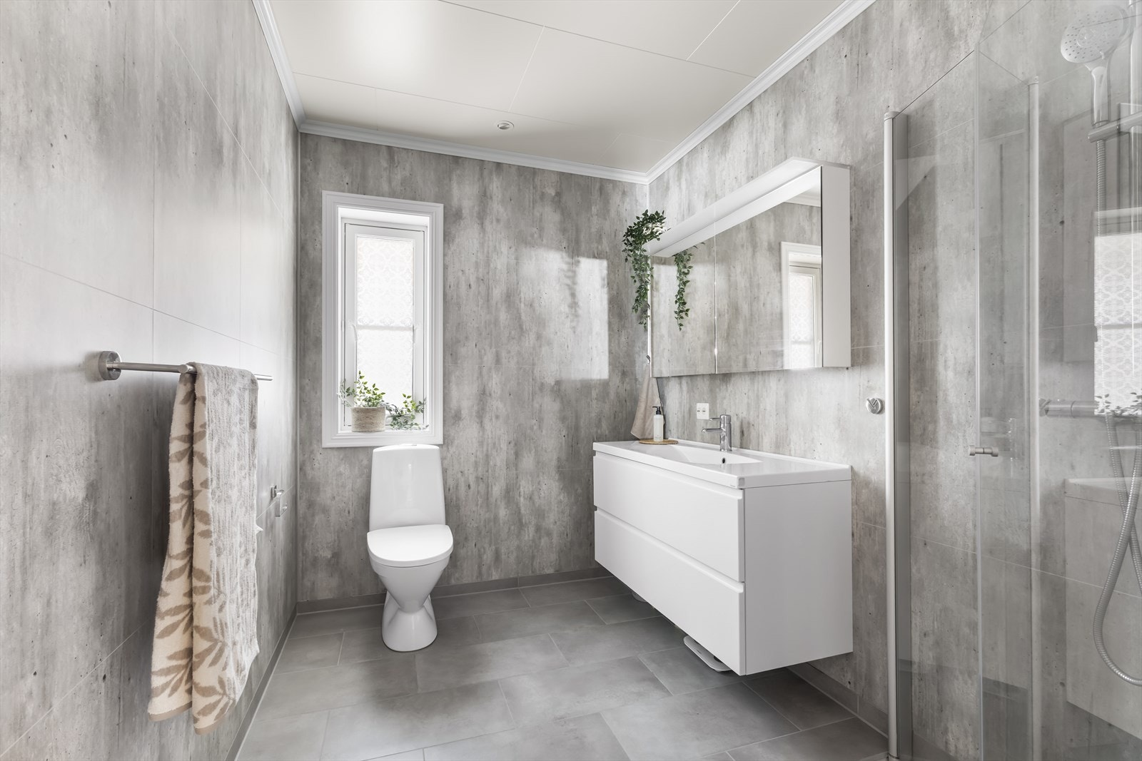 Delikat bad med våtromsplater på veggene og flislagt gulv. Badet er utstyrt med innredning med nedfelt servant og skuffer, toalett og dusjvegger. Galleribilde