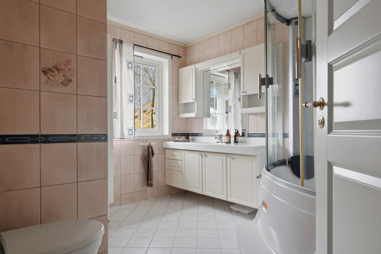 Badet er funksjonelt innredet med flislagte overflater, servant, toalett og dusjløsning. Rommet har elektriske varmekabler i gulv, noe som gir god komfort i hverdagen. Galleribilde