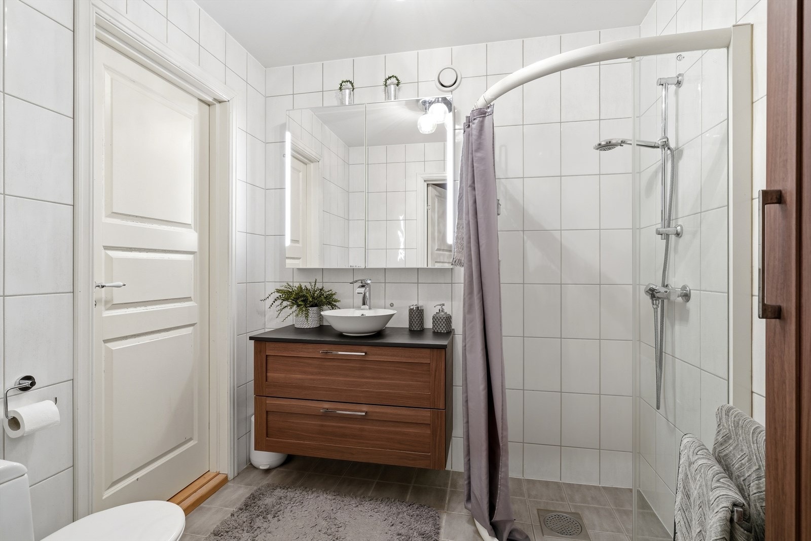 Badet er fra byggeår. Rommet har innredning med nedfelt servant, toalett og dusjvegger/hjørne. Galleribilde