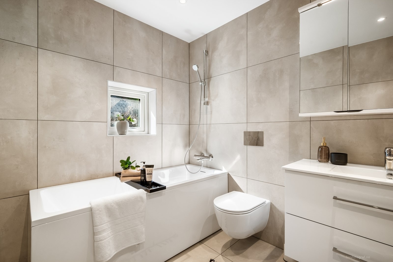 Badet i første etasje er innredet med badekar, vegghengt toalett og hvit baderomsinnredning med speilskap. Galleribilde