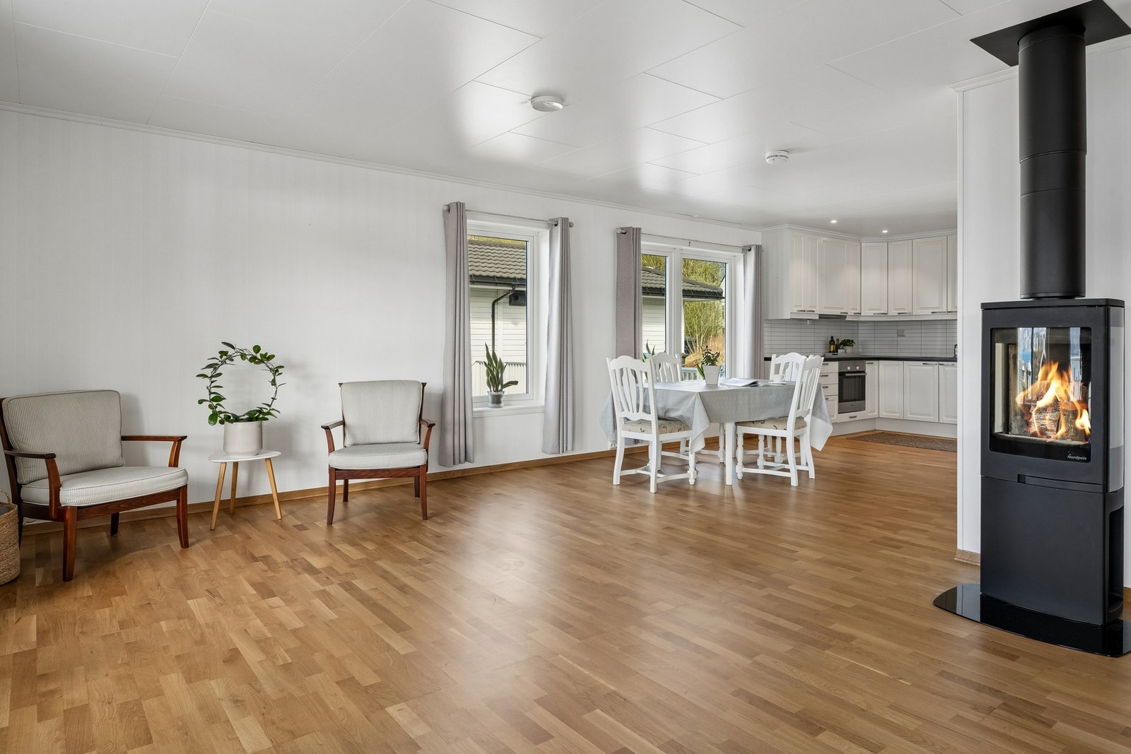 Stove og kjøkken i open løysing gjev god plass til stort spisebord. Vedomnen gjev både varme og stemning - eit naturleg midtpunkt i rommet Galleribilde