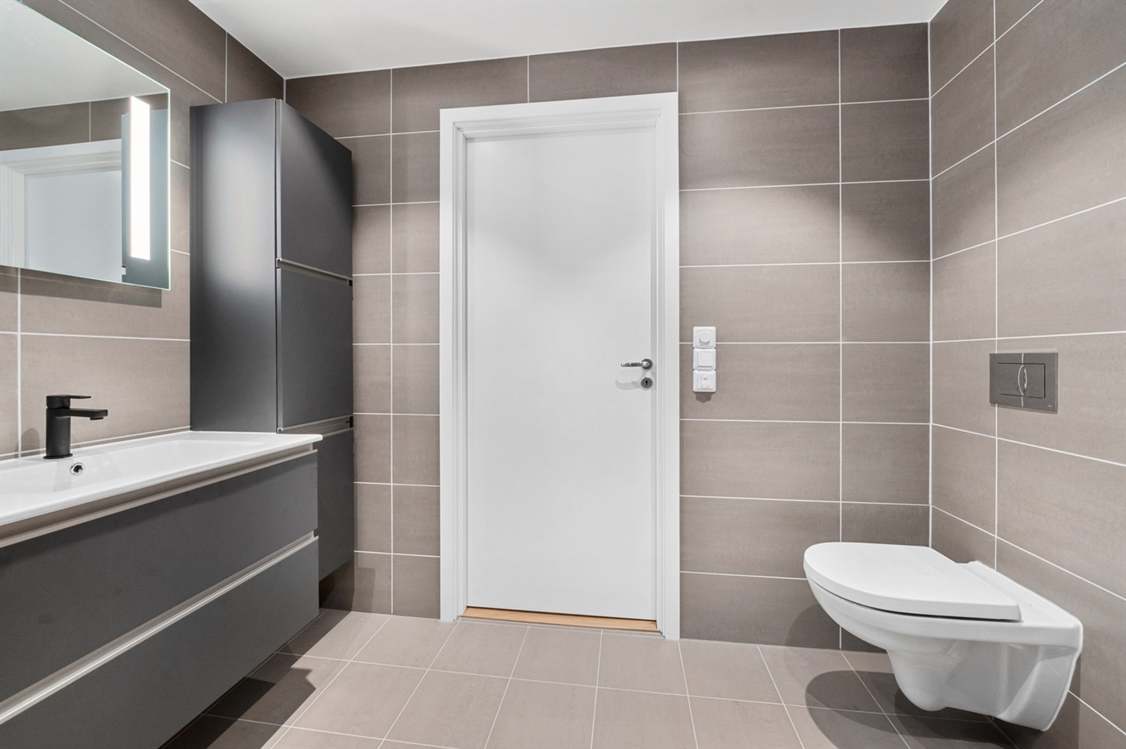 Badet måler 5 kvm og er pent flislagt med varme i gulv og lekker innredning med mørke glatte fronter. Galleribilde