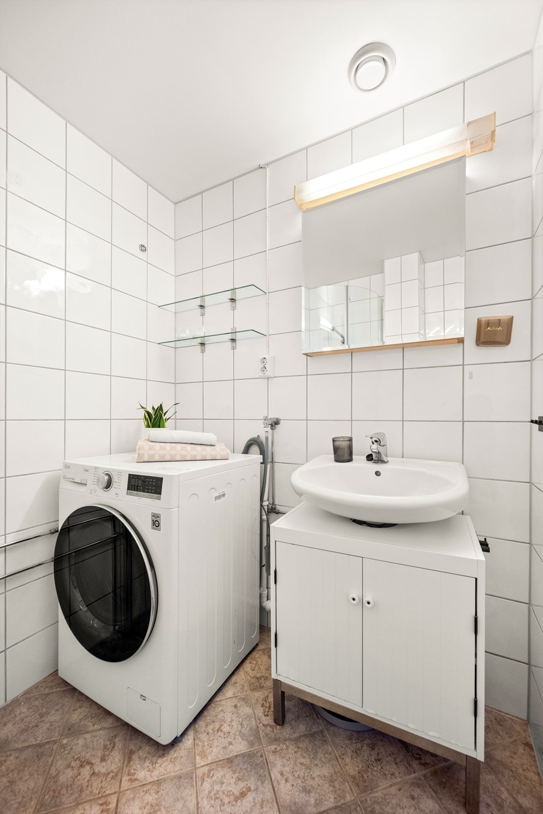 Badet er innredet med gulvstående toalett, dusjhjørne med svingbare glassdører og baderomsmøbel med servant, skap og speil med belysning. Galleribilde