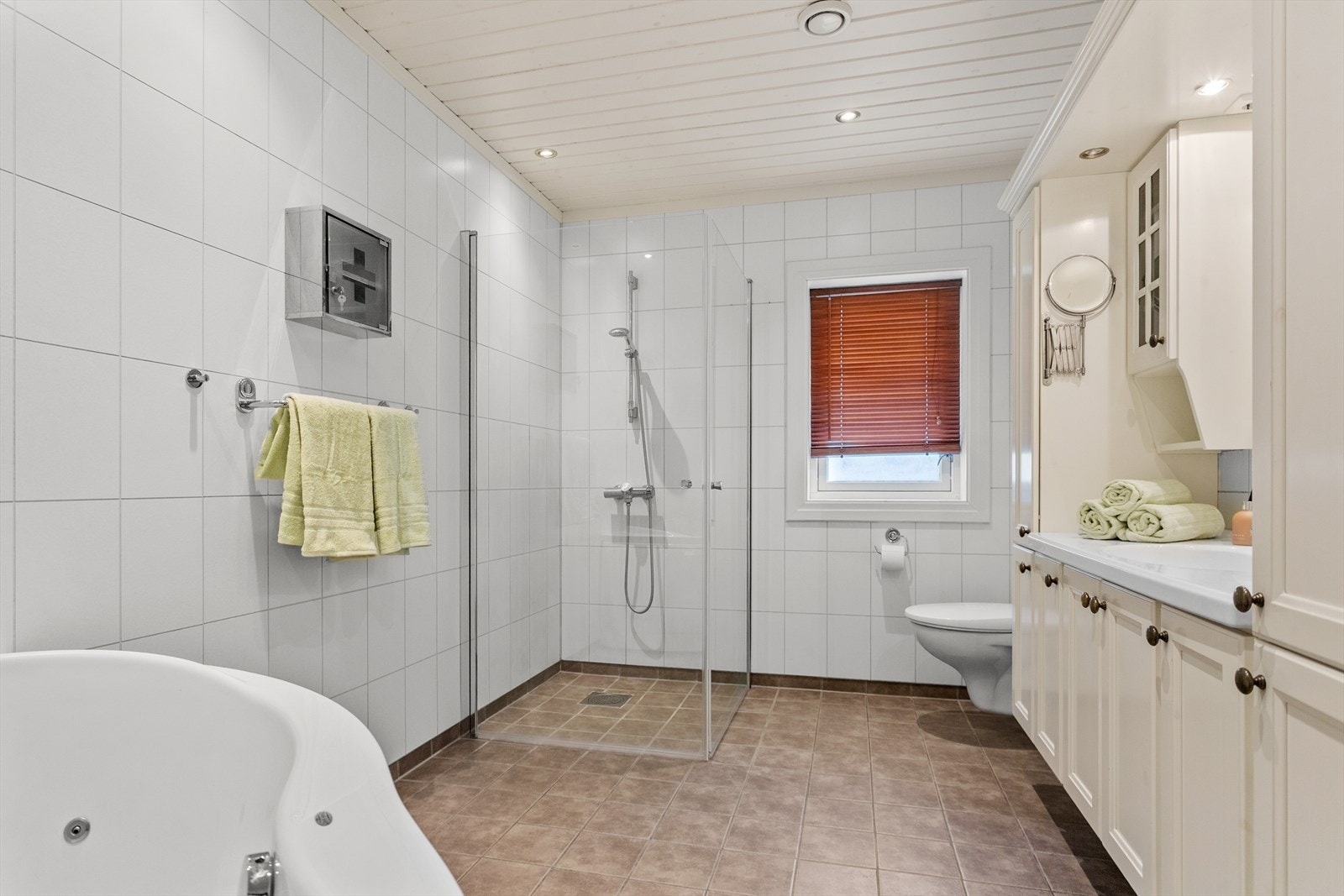 Badet i 1. etasje har flislagt gulv med undervarme, våtromsplater på vegger og malt panelhimling med downlights Galleribilde