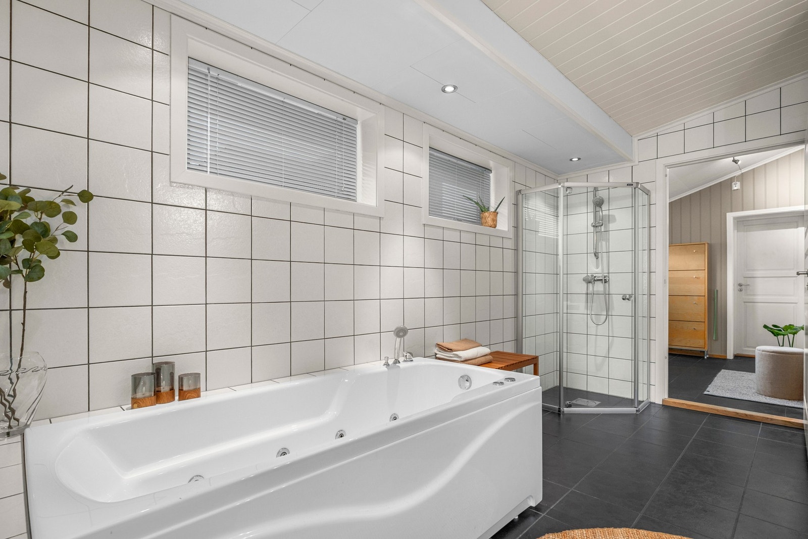 Badet er innredet med servantinnredning, veggmontert toalett, dusjhjørne og boblebadekar Galleribilde
