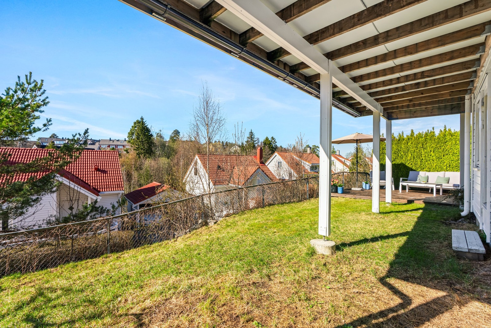 Utsikt mot nabolaget fra en overbygd terrasse med gressplen og gjerde. Galleribilde