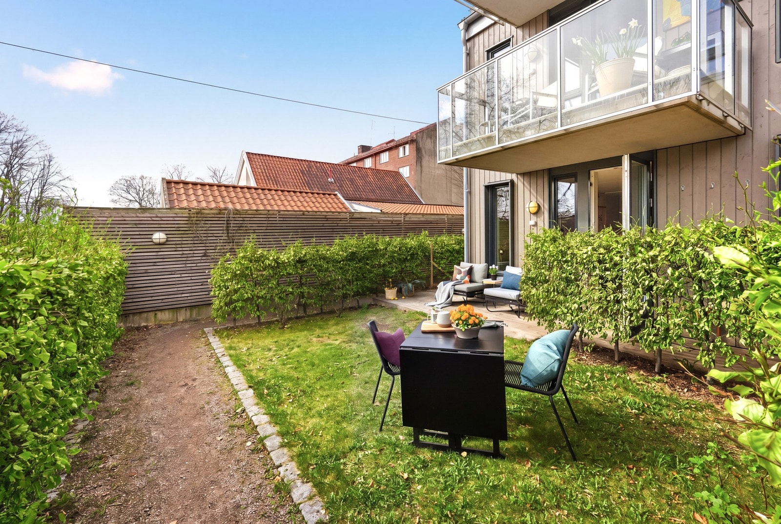 Her får du direkte adkomst til en hyggelig felleshage, skjermet av en frodig hekk som gir en lun og privat atmosfære. Bildet er KI-generert som sommerbilde. Galleribilde
