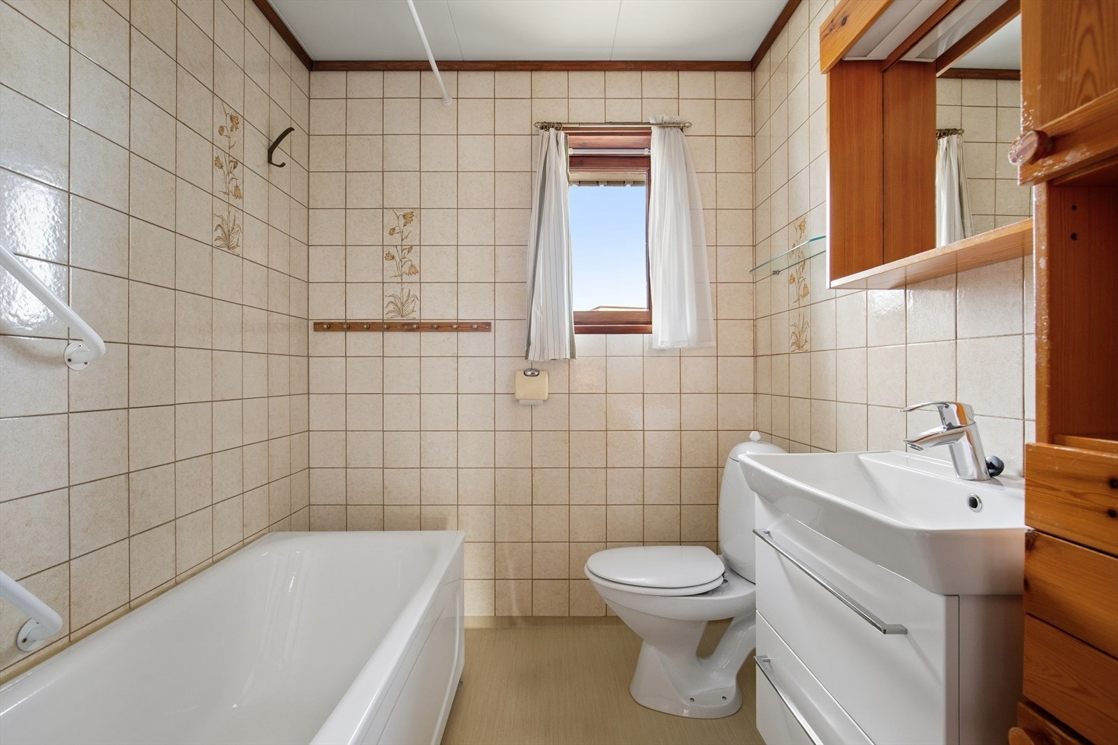 Badet er fra byggeår og er innredet med lyse, sjatterte fliser på vegg og vinylbelegg på gulv. I gulvet har man også varmekabler for ekstra komfort. Badet er ellers utstyrt med badekar, toalett og nyere baderomsinnredning med servant. Galleribilde