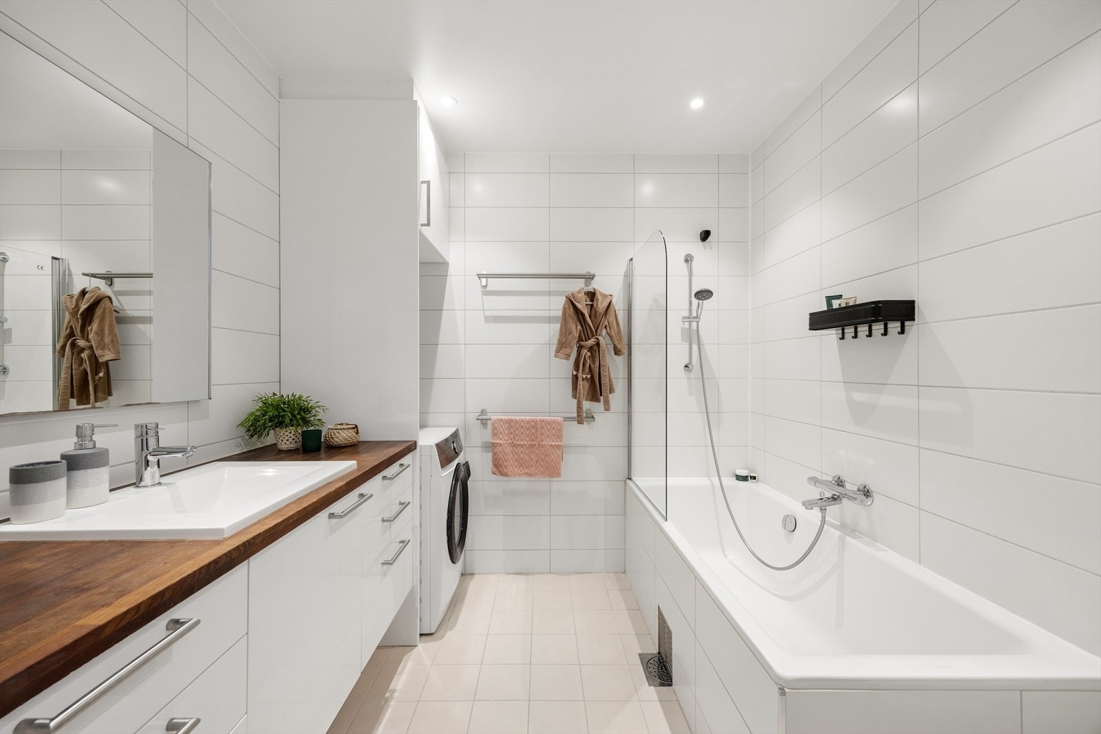 Moderne og fint baderom innredet med benkeplate med innfelt servant, underskap, speil med integrert belysning, innebygget badekar med dusj og veggmontert toalett. Opplegg for vaskemaskin Galleribilde