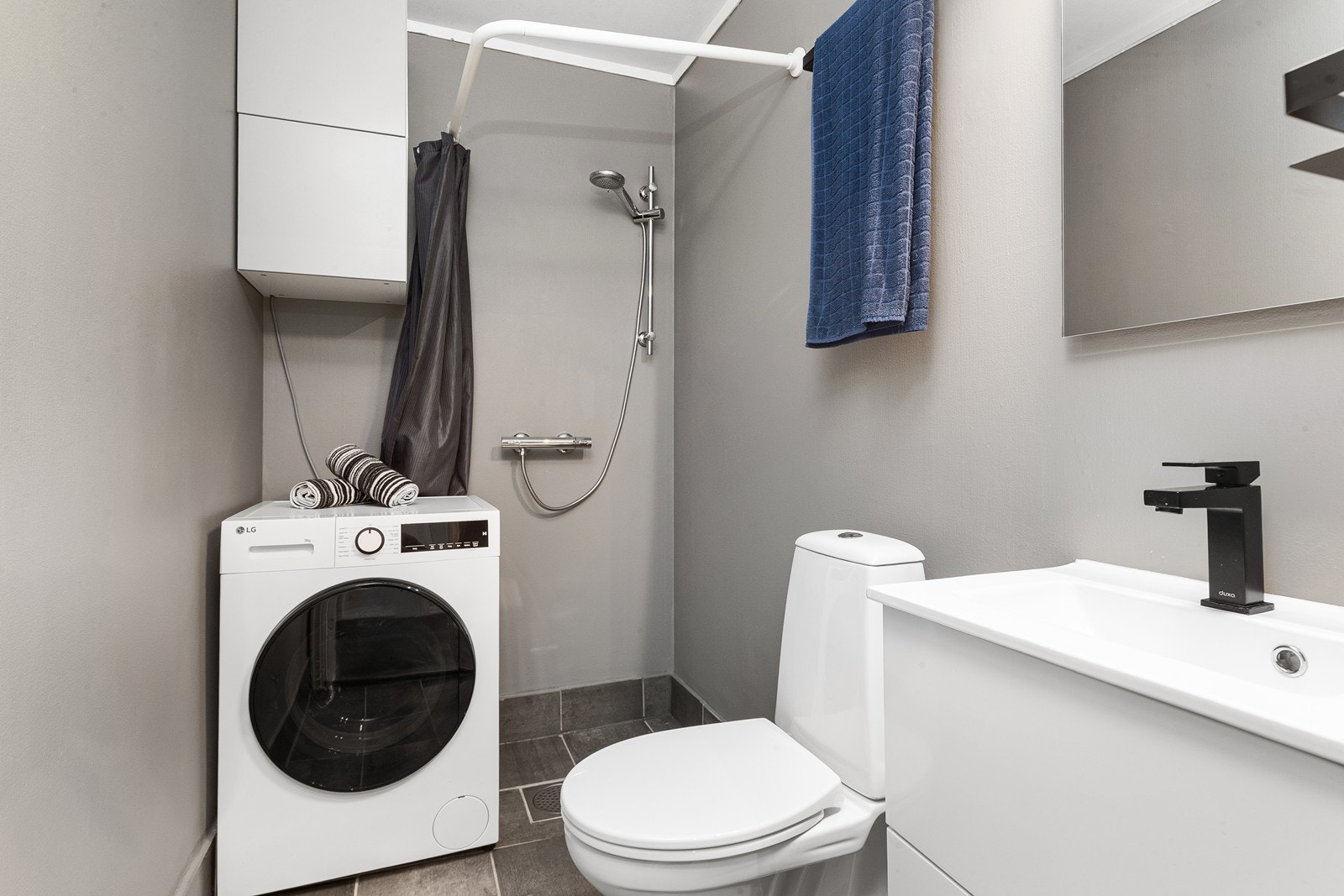 Badet har flislagt gulv og vegger med malte plater. Rommet er utstyrt med toalett, dusjhjørne, servant med underskap samt opplegg for vaskemaskin. Galleribilde