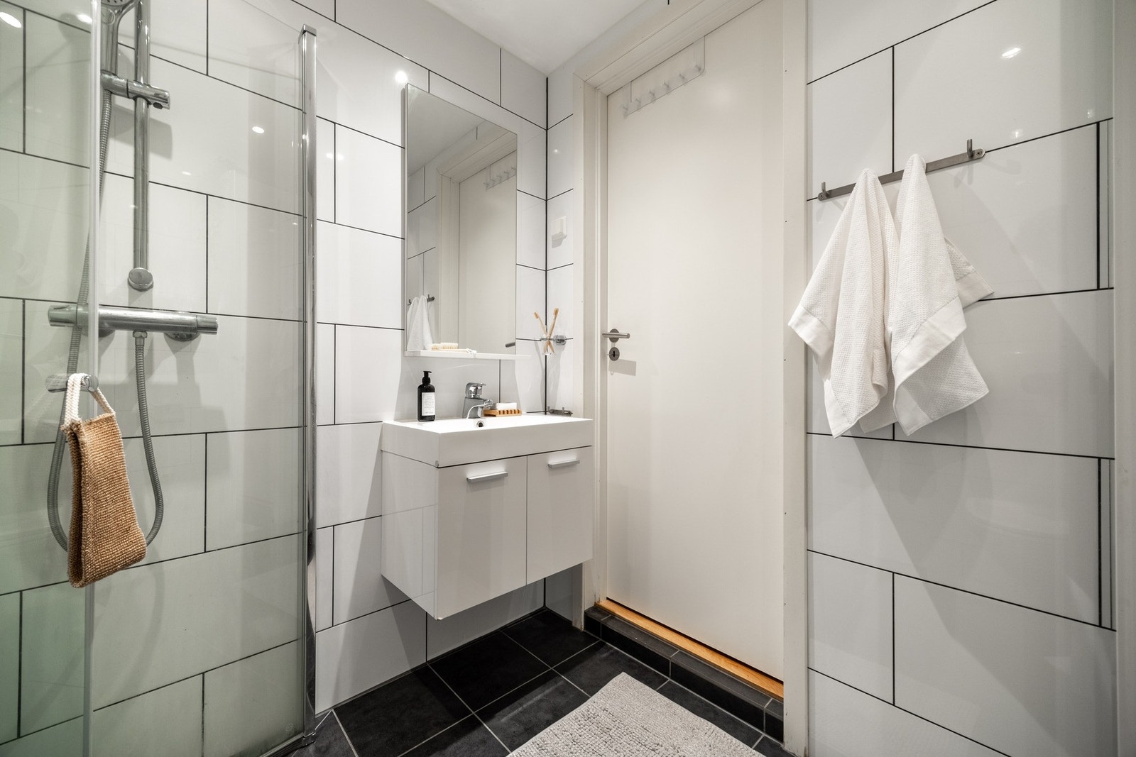 Badet er utstyrt med vegghengt servant med skap, dusjhjørne med innfellbare vegger, og vegghengt toalett. Galleribilde