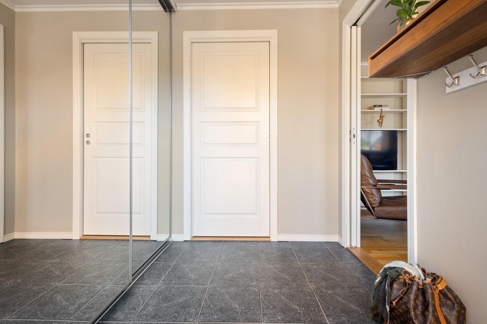 Entré med flislagt gulv med varmekabler og skyvedørsgarderobe med speil. Galleribilde