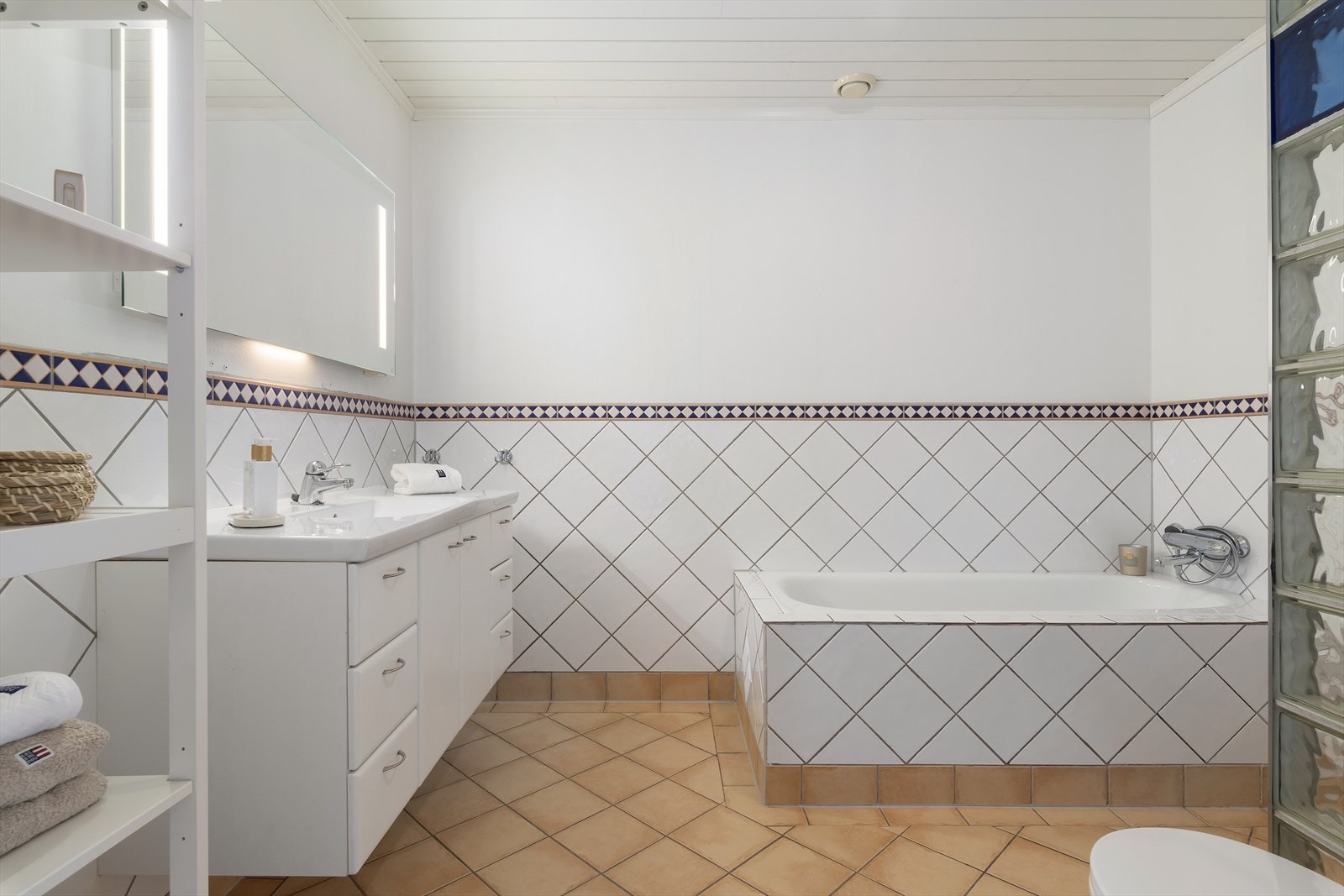 Bad med flis på gulv og til brystning. Her er innefliset badekar, dusjnisje, toalett, innredning med helstøpt servantplate og speil med lys. Galleribilde