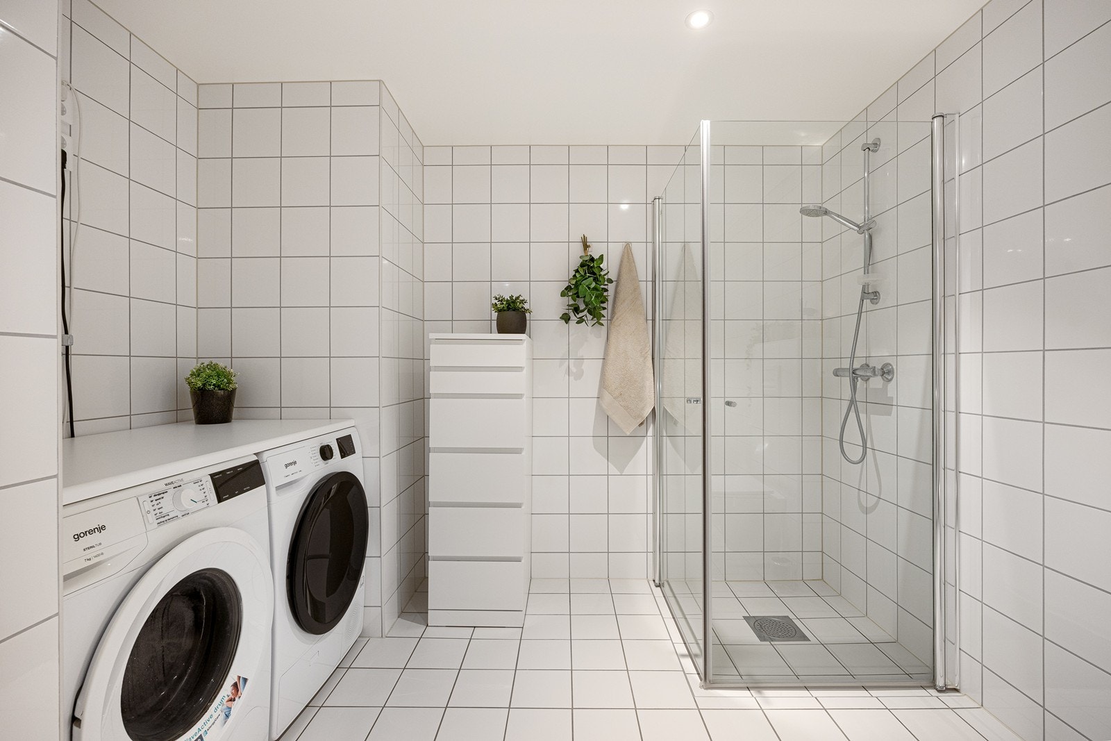 Badet er utstyrt med et vegghengt toalett, opplegg for vaskemaskin og et dusjhjørne med innfellbare glassdører. Galleribilde