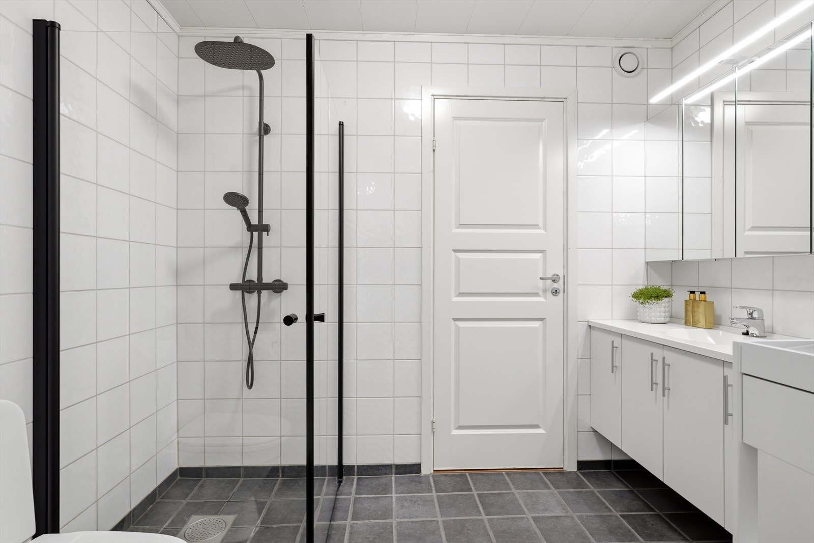 Badet har flislagt gulv og vegger, og det er elektrisk gulvvarme. Badet inneholder stor innredning med heldekkende servant, speilskap, toalett og dusjhjørne. Galleribilde