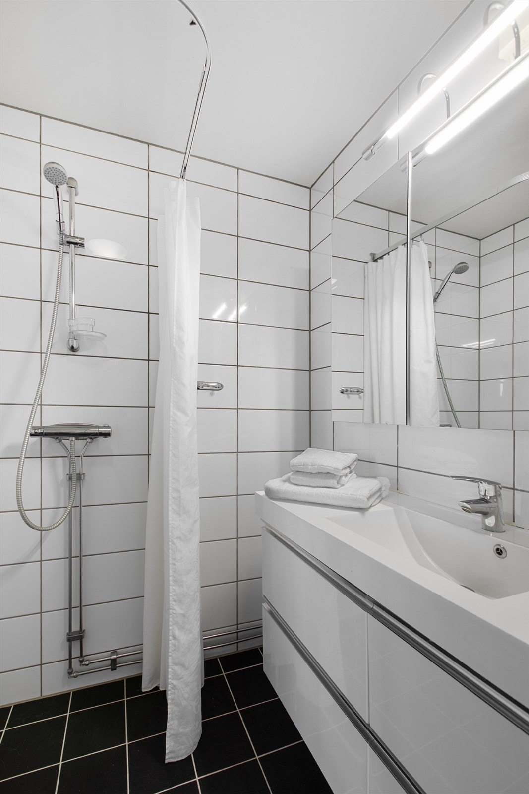 Badet er utstyrt med dusj, baderomsinnredning med servant og speilskap. Galleribilde