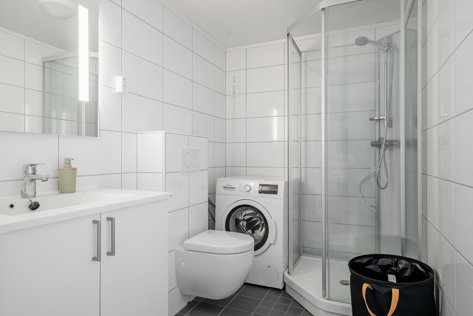 Badet i utleiedelen har flislagte vegger og gulv, med elektriske varmekabler. Rommet er innredet med nedfelt servant over skap, speil med integrert belysning, vegghengt toalett, dusjkabinett og opplegg for vaskemaskin. Galleribilde
