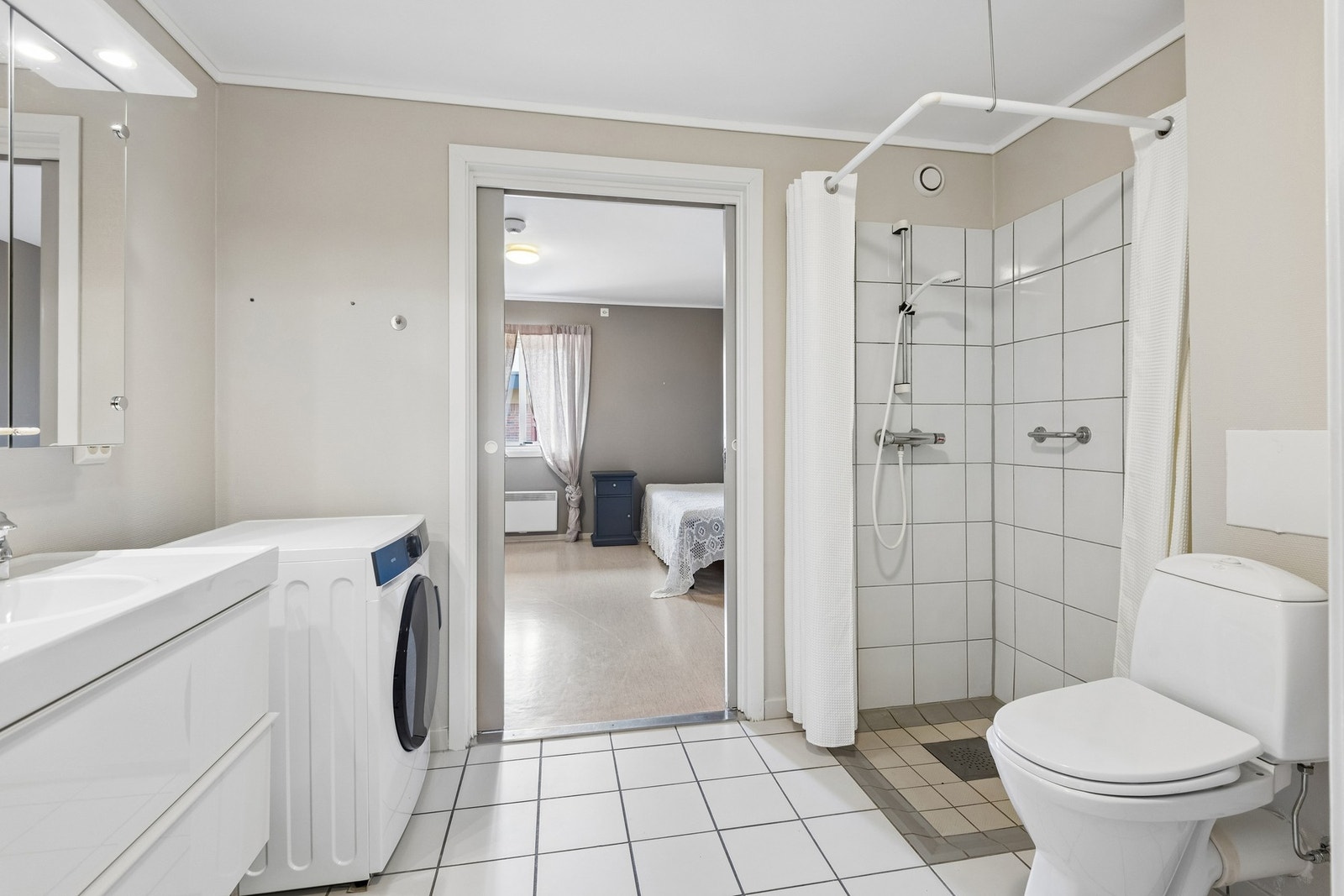 Flislagt bad med dusjhjørne og opplegg for vaskemaskin. Badet ligger praktisk til med adkomst både fra soverommet og gangen. Galleribilde