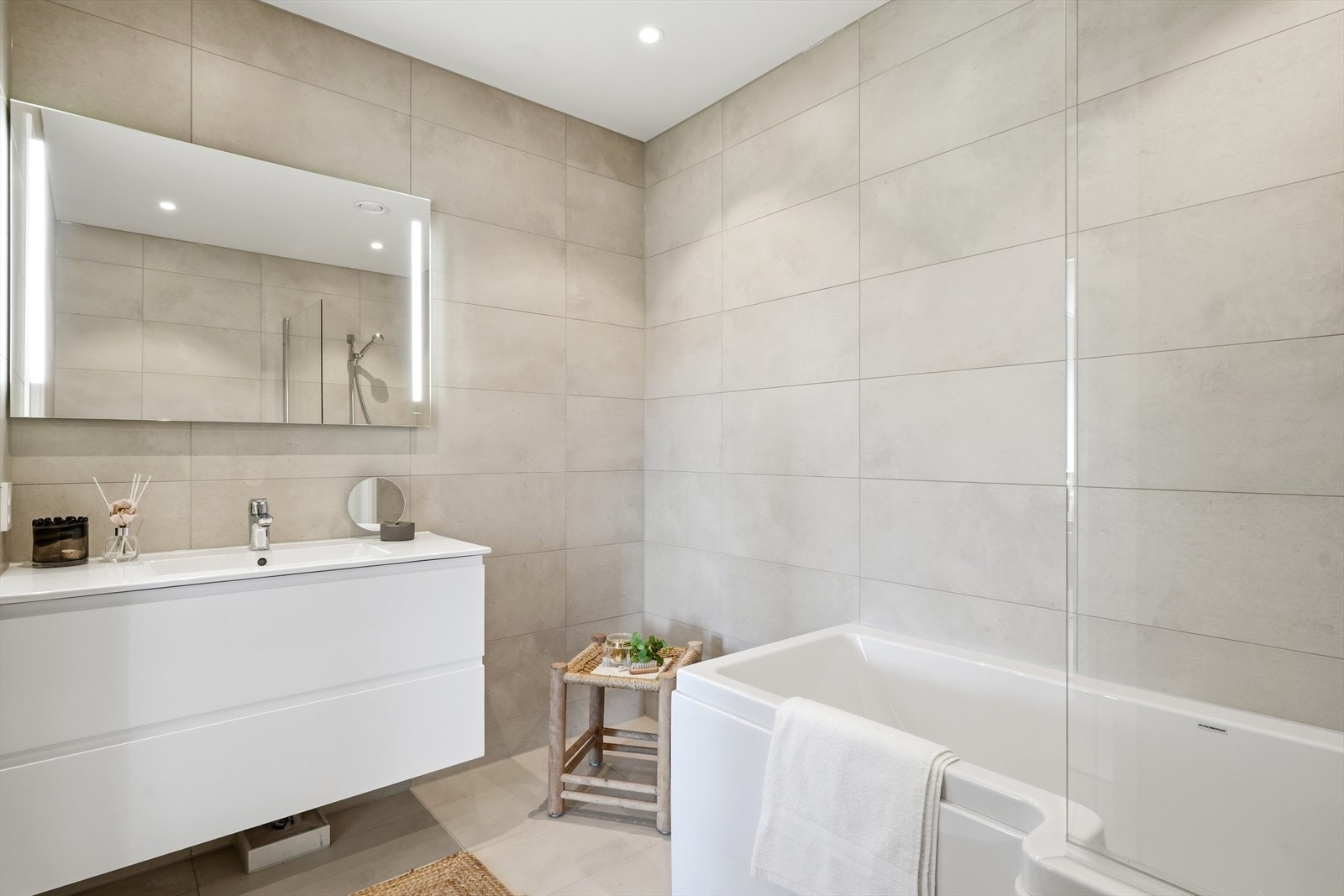 Hovedbadet er også flislagt med delikate fliser på gulv og vegger, og det er elektrisk gulvvarme. Badet inneholder innredning med heldekkende servant, veggmontert toalett og badekar med dusjgarnityr. Galleribilde