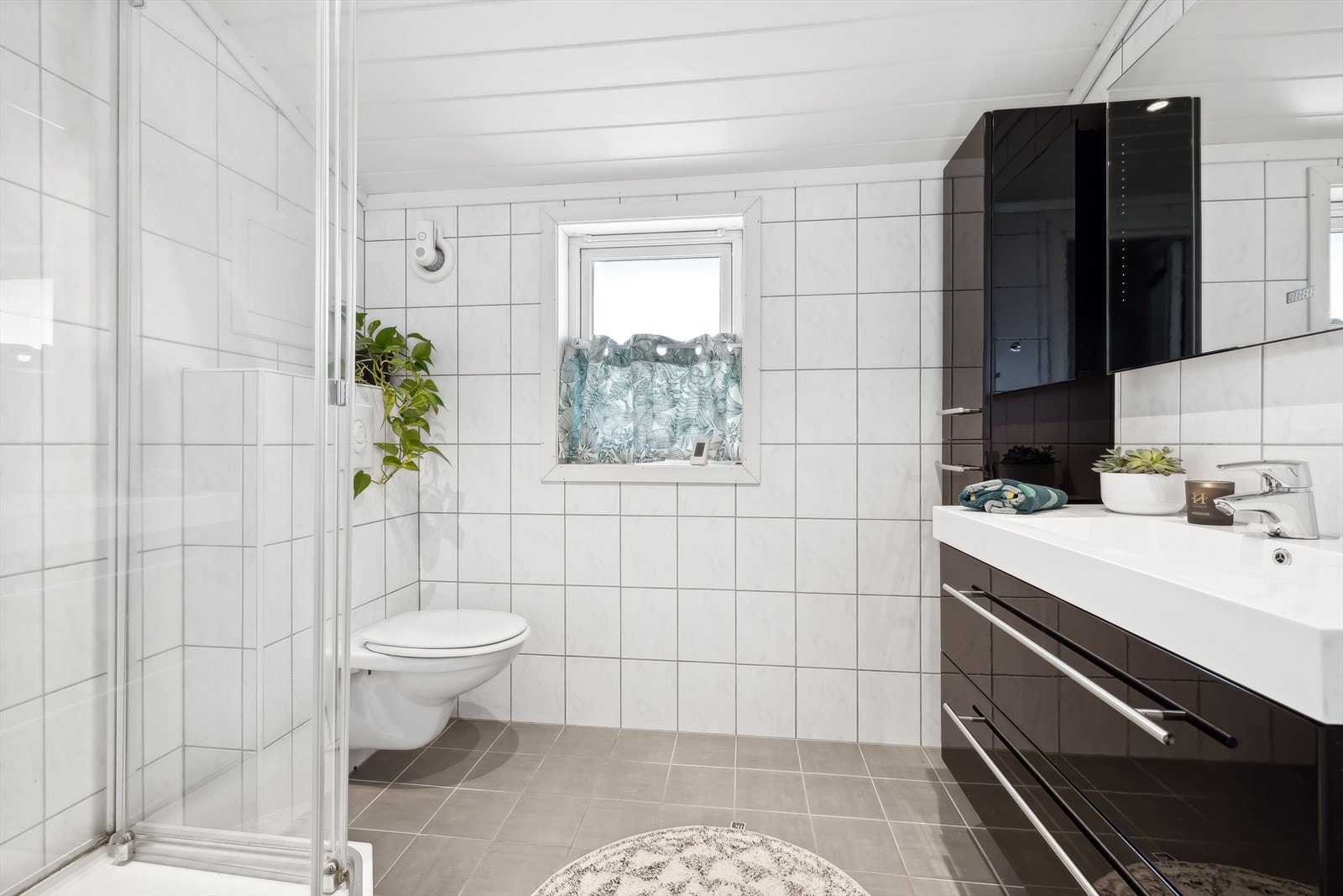 Badet har dusjkabinett, servant med moderne innredning og skuffer, speil med innfelt lys, høyskap og vegghengt toalett. Galleribilde