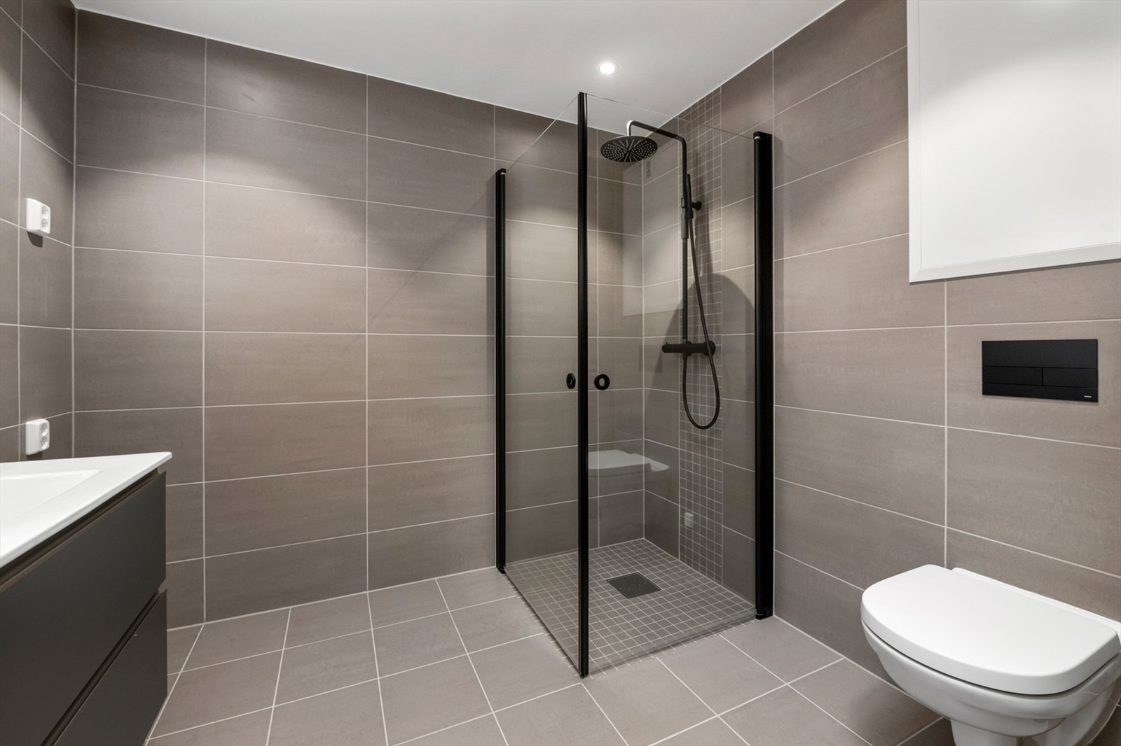 Badet inneholder servantskap, speil med innebygd lys, vegghengt toalett og dusjhjørne med innfellbare vegger. Galleribilde