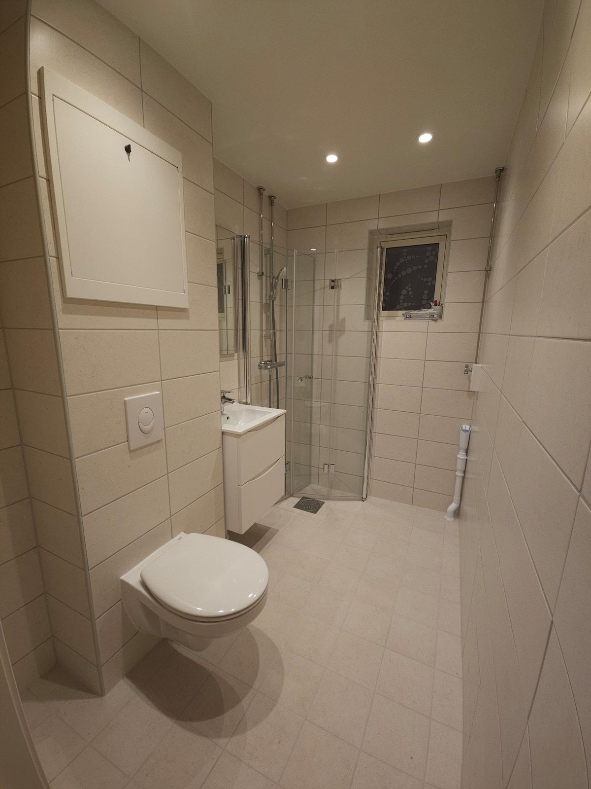 Innredningen består av vegghengt toalett, servant med underskap, speil og dusjhjørne med innfellbare dusjvegger. Downlight i himling for å styre lysstyrken (privat foto). Galleribilde