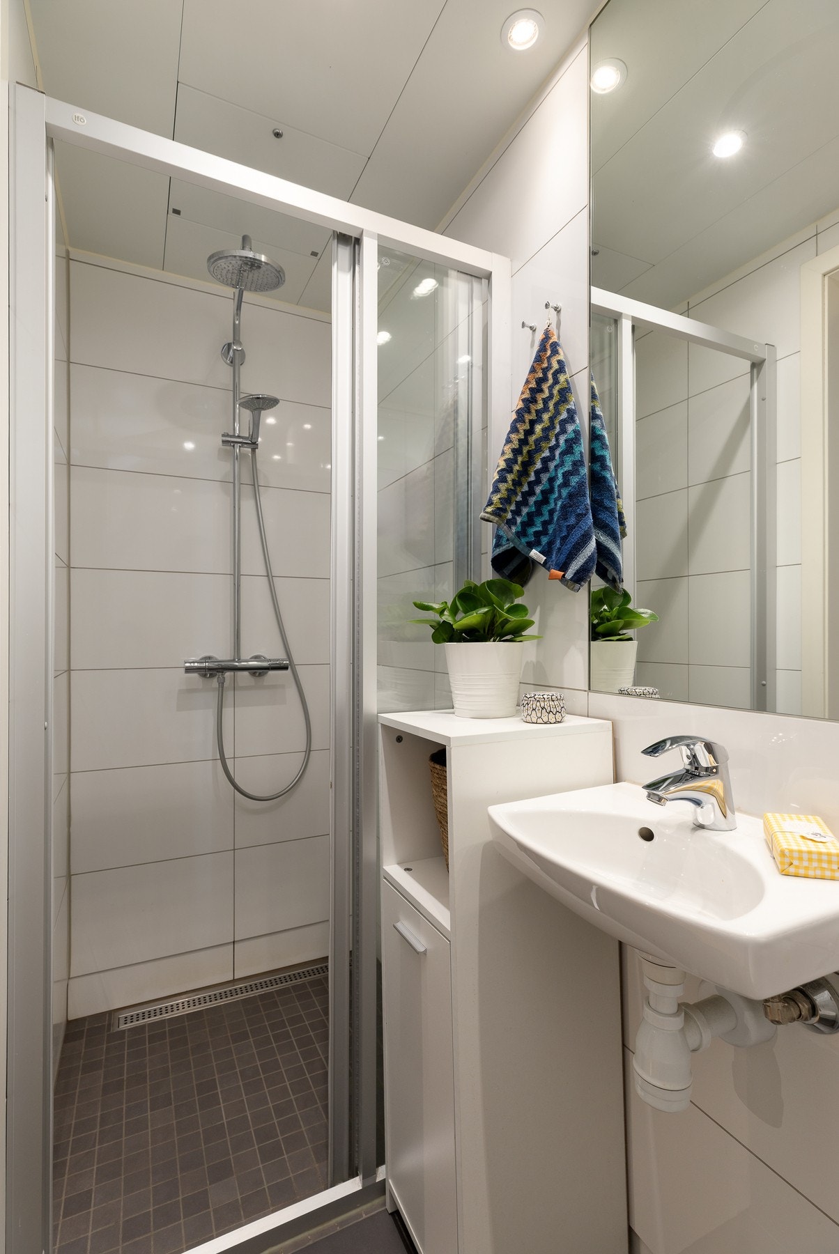 Badet inneholder dusj med faste glassfelt og skyvedør, vegghengt toalett med innebygget sisterne, samt servant med speil. Galleribilde