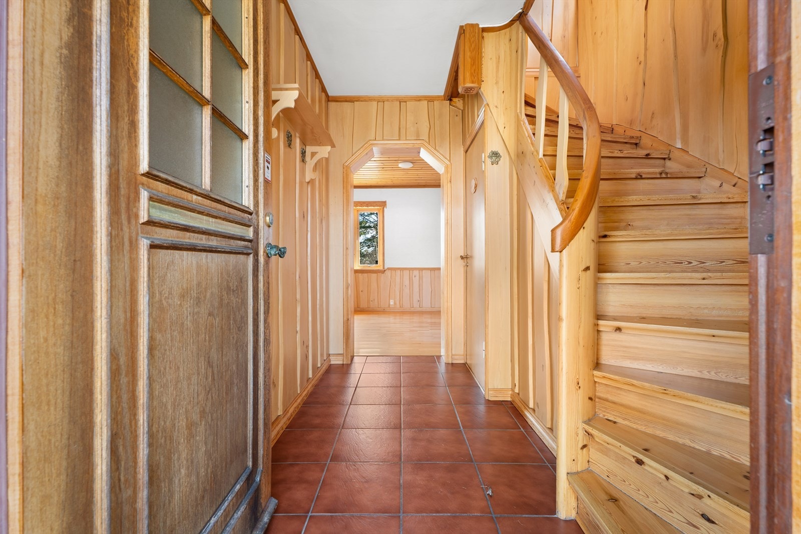 Entré med flislagt gulv og panel på veggene. Den lakkerte furutrappen leder opp til andre etasje. Galleribilde
