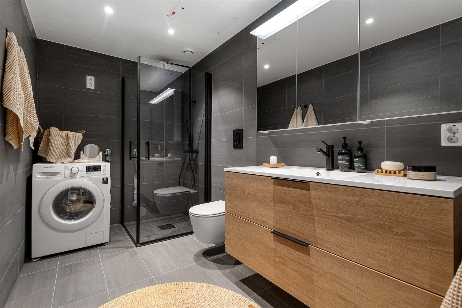 Badet har vegghengt toalett fra Grohe. Både vegger og gulv er belagt med delikate fliser. I dusjsonen er det nedfelte fliser i tilsvarende kvalitet og farge i format 5x5 cm for et helhetlig uttrykk. Galleribilde