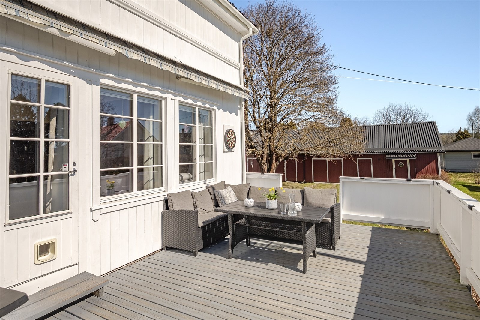 Sørvendt treterrasse med adkomst fra stuen. Tett rekkverk kledd med stående bordkledning, så her sitter du skjermet og fint til i solveggen. Galleribilde