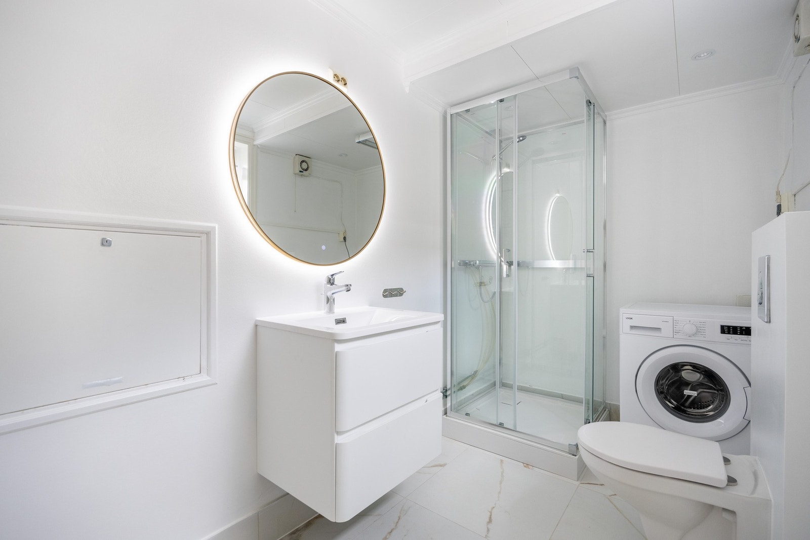 Badet er utstyrt med skap med glatte fronter, speil med belysning over servanten, klosett, dusjkabinett og opplegg for vaskemaskin. Galleribilde