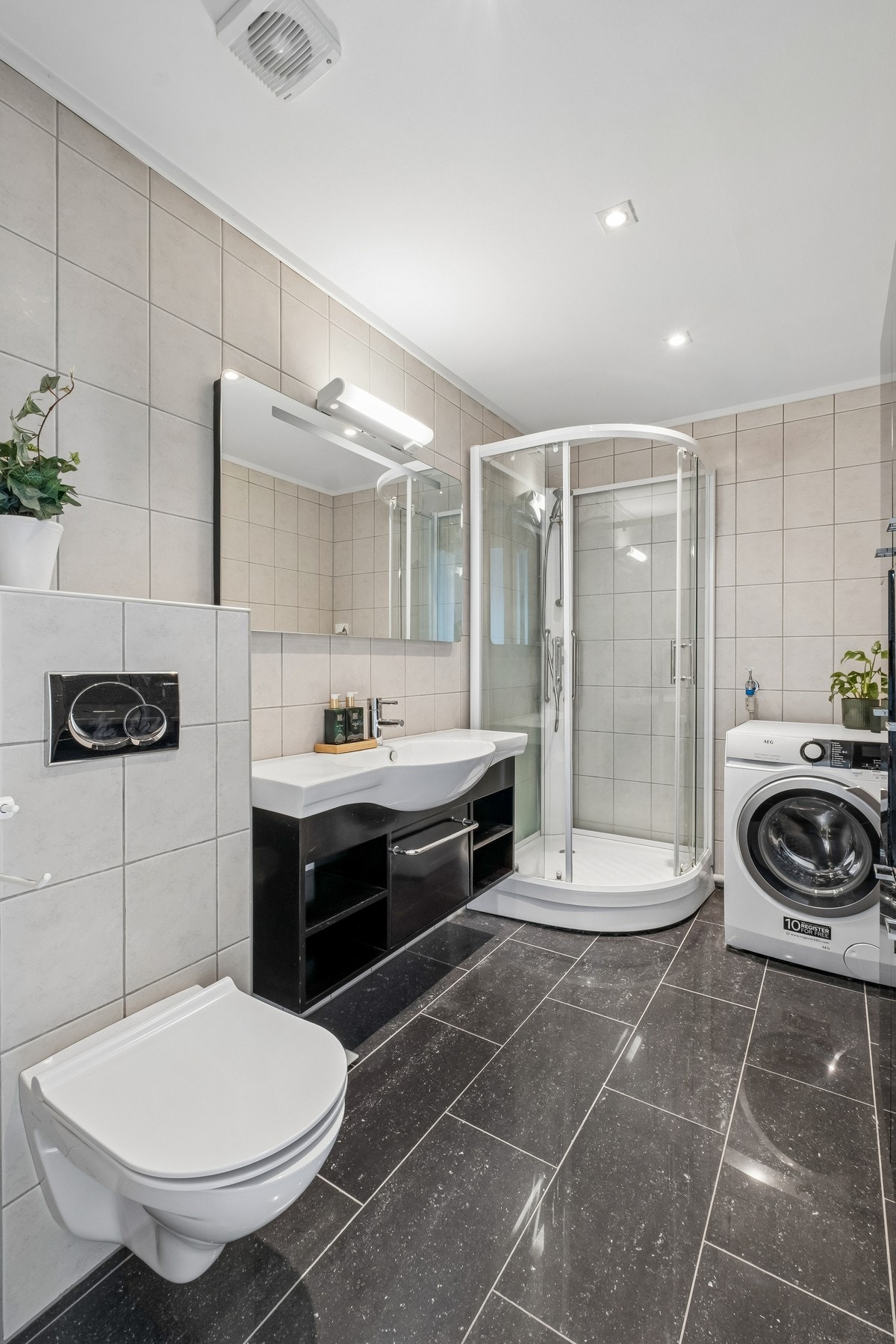 Pent flislagt bad med elektriske varmekabler i gulv. Badet er innredet med vegghengt toalett, dusjkabinett, servant på skuffeseksjon og opplegg for vaskemaskin. Galleribilde