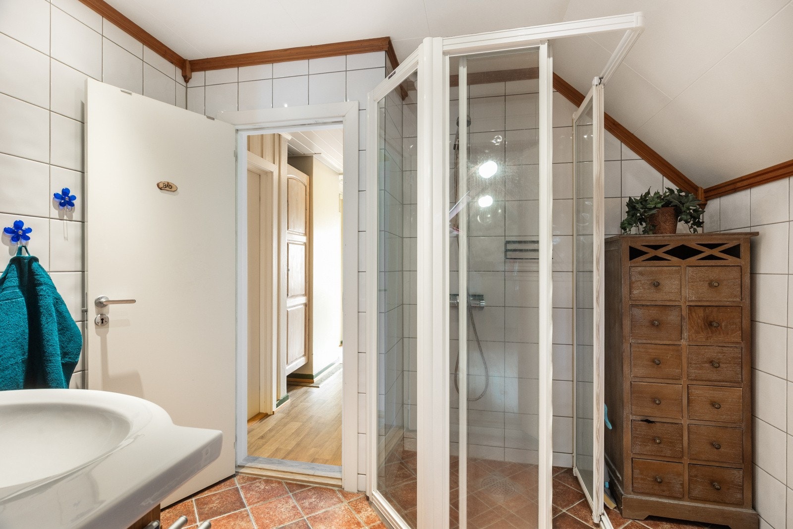 Badet er utstyrt med dusjhjørne med innfellbare vegger, servantinnredning og høyskap. Rommet har elektrisk styrt avtrekksvifte. Galleribilde