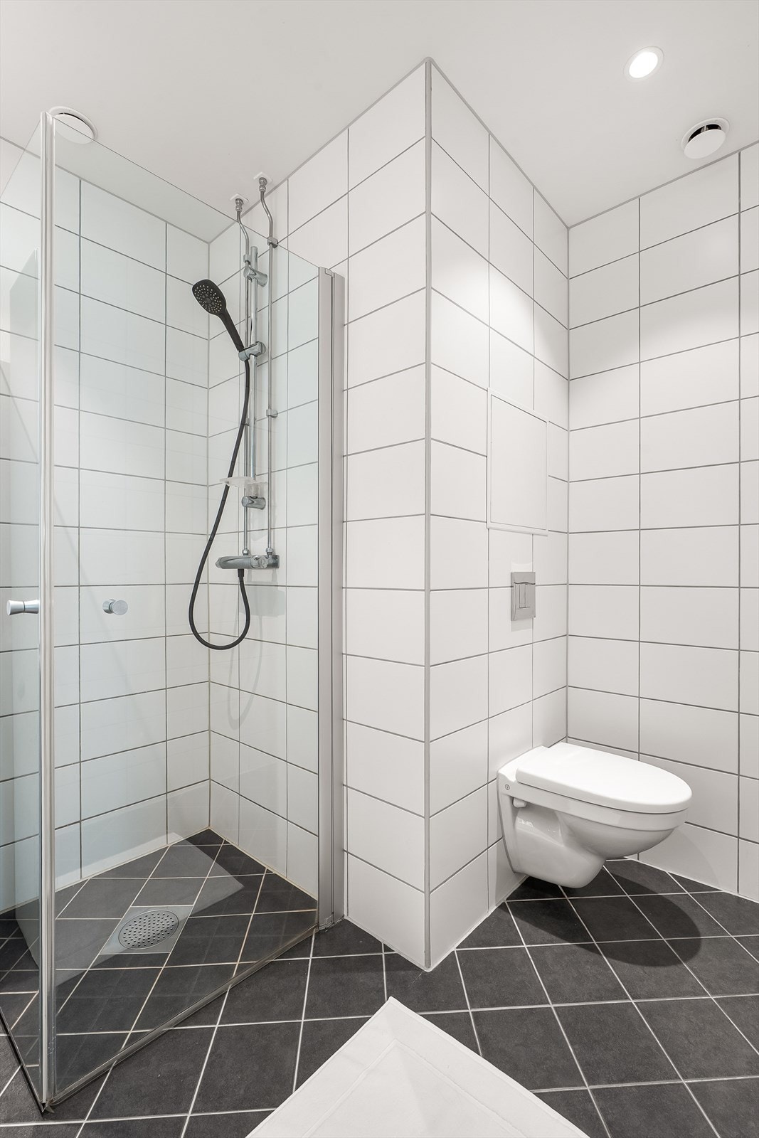 Videre er badet innredet med gulvvarme, downlights i himling, vegghengt klosett, servant nedfelt i innredning og dusjhjørne med svingbare glassdører. Galleribilde
