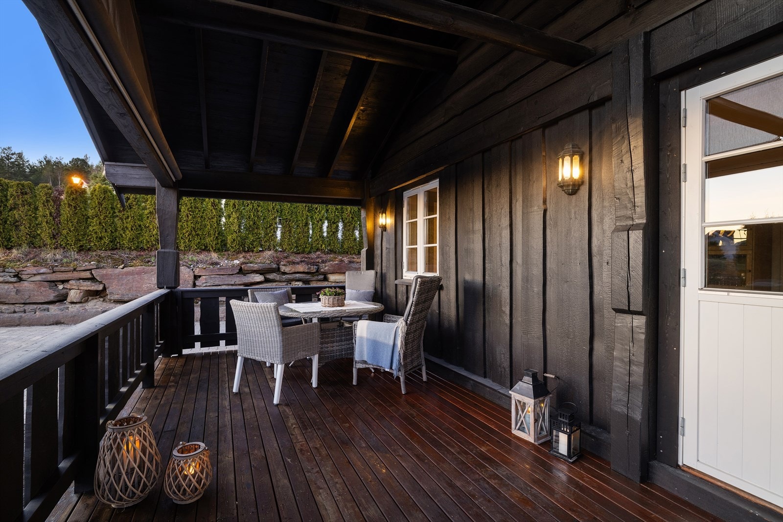 Terrassen har et spaltegulv av terrassebord under tak, og er rammet inn av et solid rekkverk i tre. Galleribilde