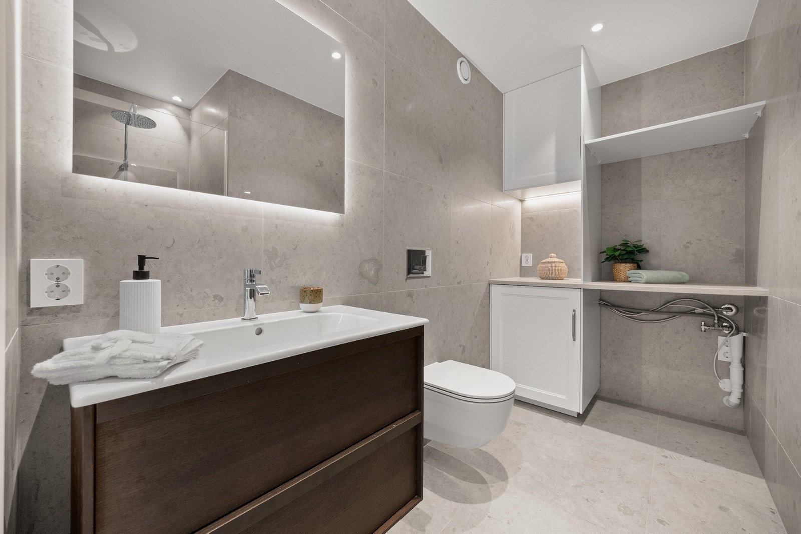 Badet er innredet med dusjnisje, servant med skuffeseksjon, vegghengt klosett og skapinnredning med avsatt plass for vaskemaskin. Galleribilde