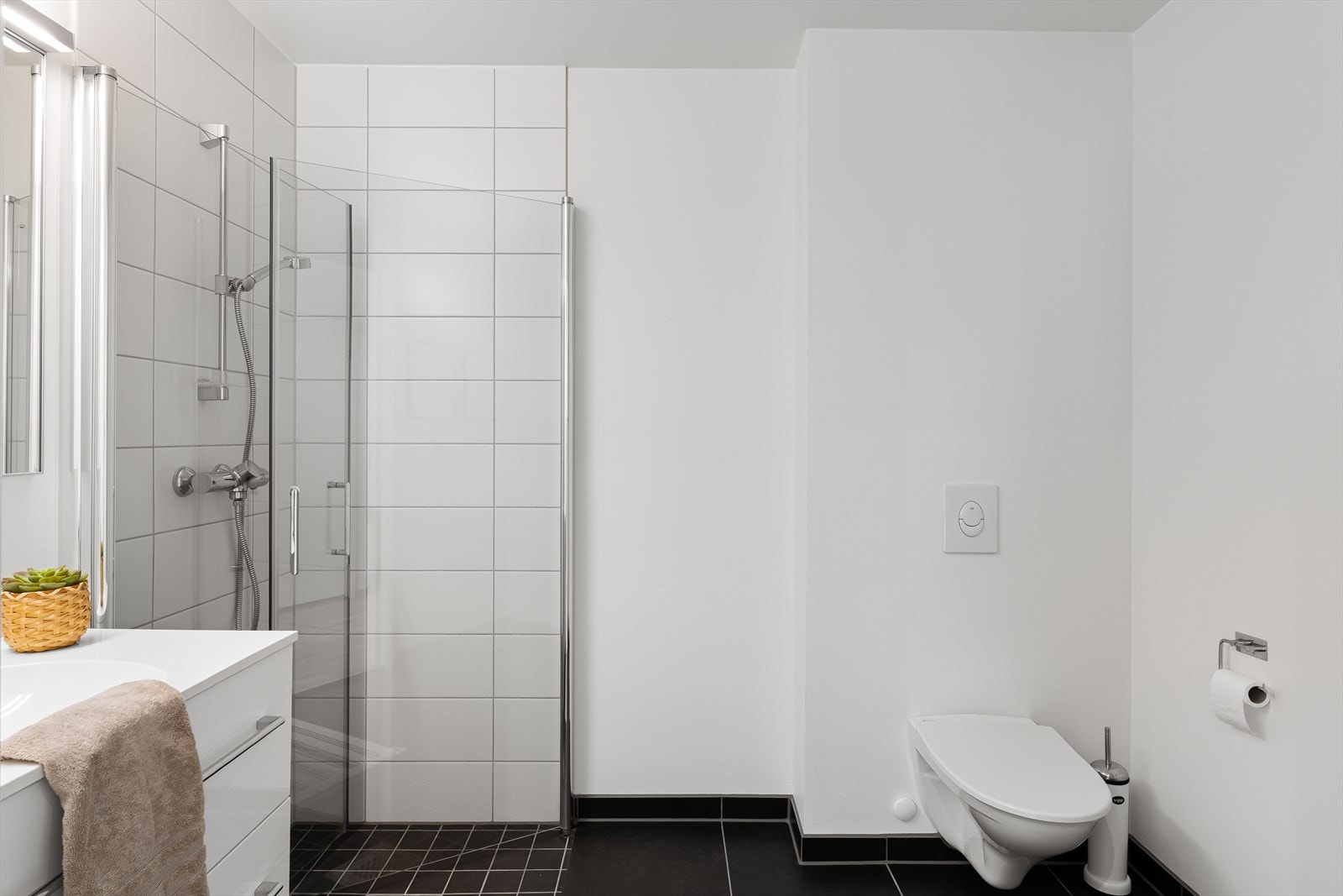 Dette badet er praktisk plassert ved entréen og har veggmontert toalett og dusjhjørne. Galleribilde