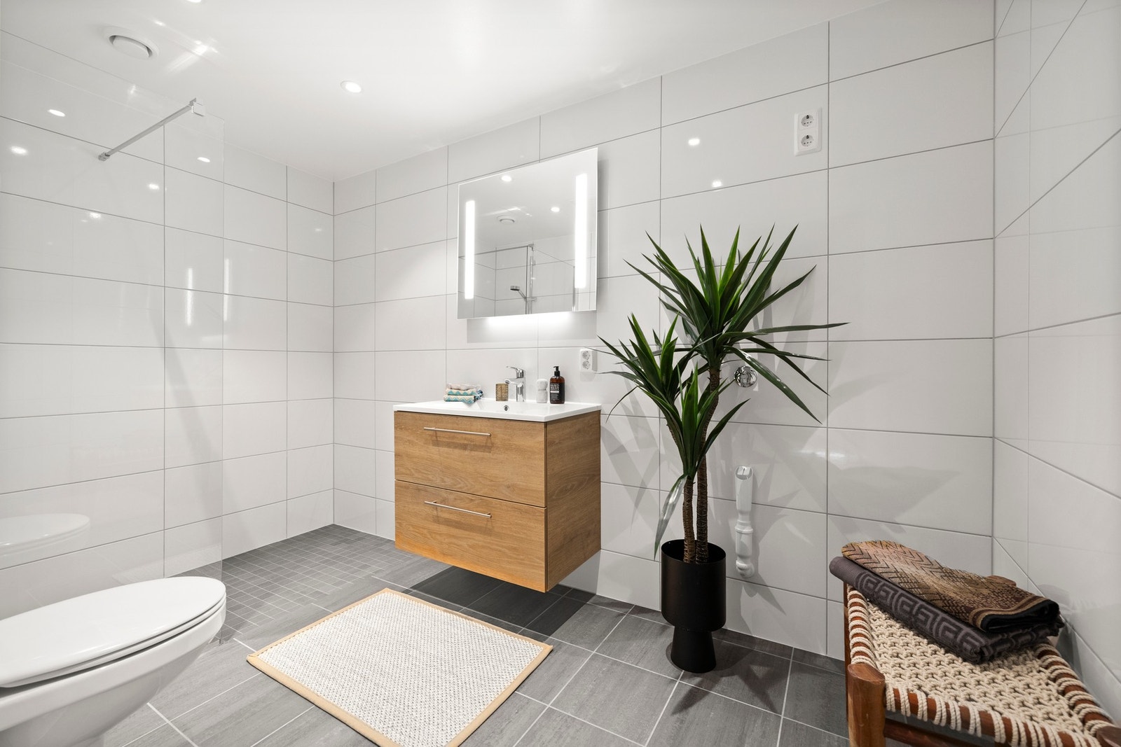 Badet er innredet med moderne og gjennomtenkte løsninger, med servantinnredning med gode oppbevaringsmuligheter og stilrene detaljer. Flislagte overflater i en kombinasjon av lyse vegger og mørkere gulv gir et tidløst og delikat uttrykk. Galleribilde