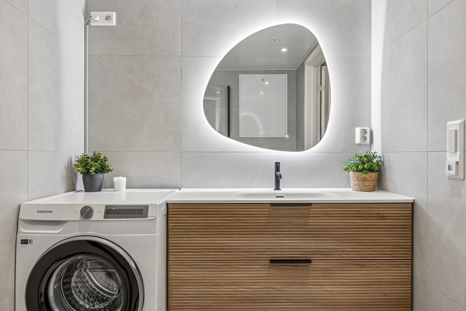 Badet er innredet med servantinnredning, opplegg for vaskemaskin, speil med lys, dusjhjørne med vegger og vegghengt toalett. Galleribilde