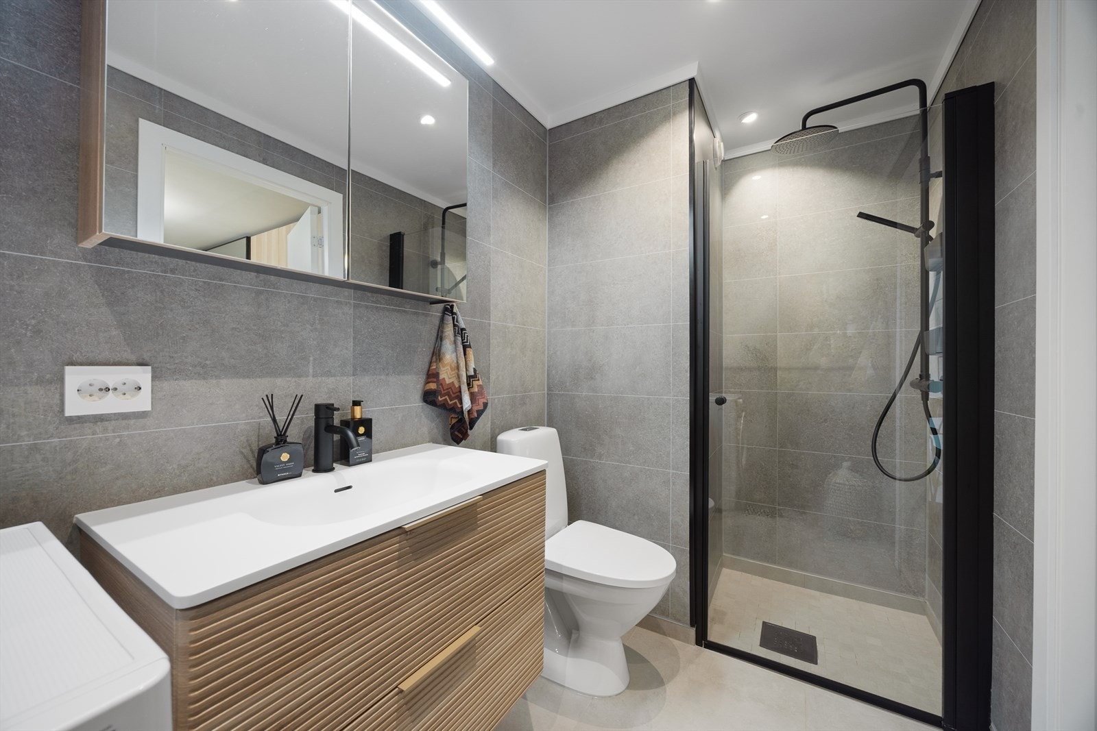 Badet er utstyrt med dusjnisje med glassdør, toalett, servantinnredning med god oppbevaringsplass, speilskap samt opplegg for vaskemaskin. Galleribilde